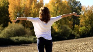 Person stood on a hill in front of trees and stretching their arms to the side