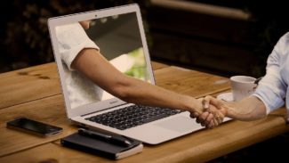 Image shows a laptop on a table with two people shaking hands