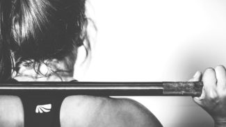 View of a woman's back and head as she rests a barbell on her shoulders