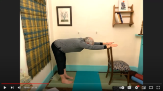 Geoff Lindsay yoga teacher stands and bends forward at the hips to stretch his back and rest his palms on a chair back