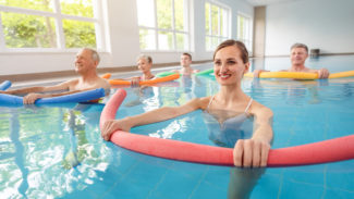 Five people in a swimming pool doing some exercises holding some floats.