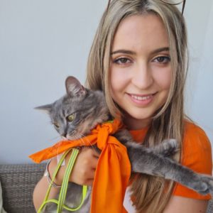 Image of Kate Liberty wearing her NASS T-shirt and holding her cat who is wearing a a NASS bandana