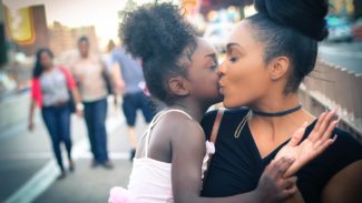 A woman is holding her daughter and kisses her cheek
