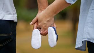 Two people hold hands and hold a small pair of shoes between them