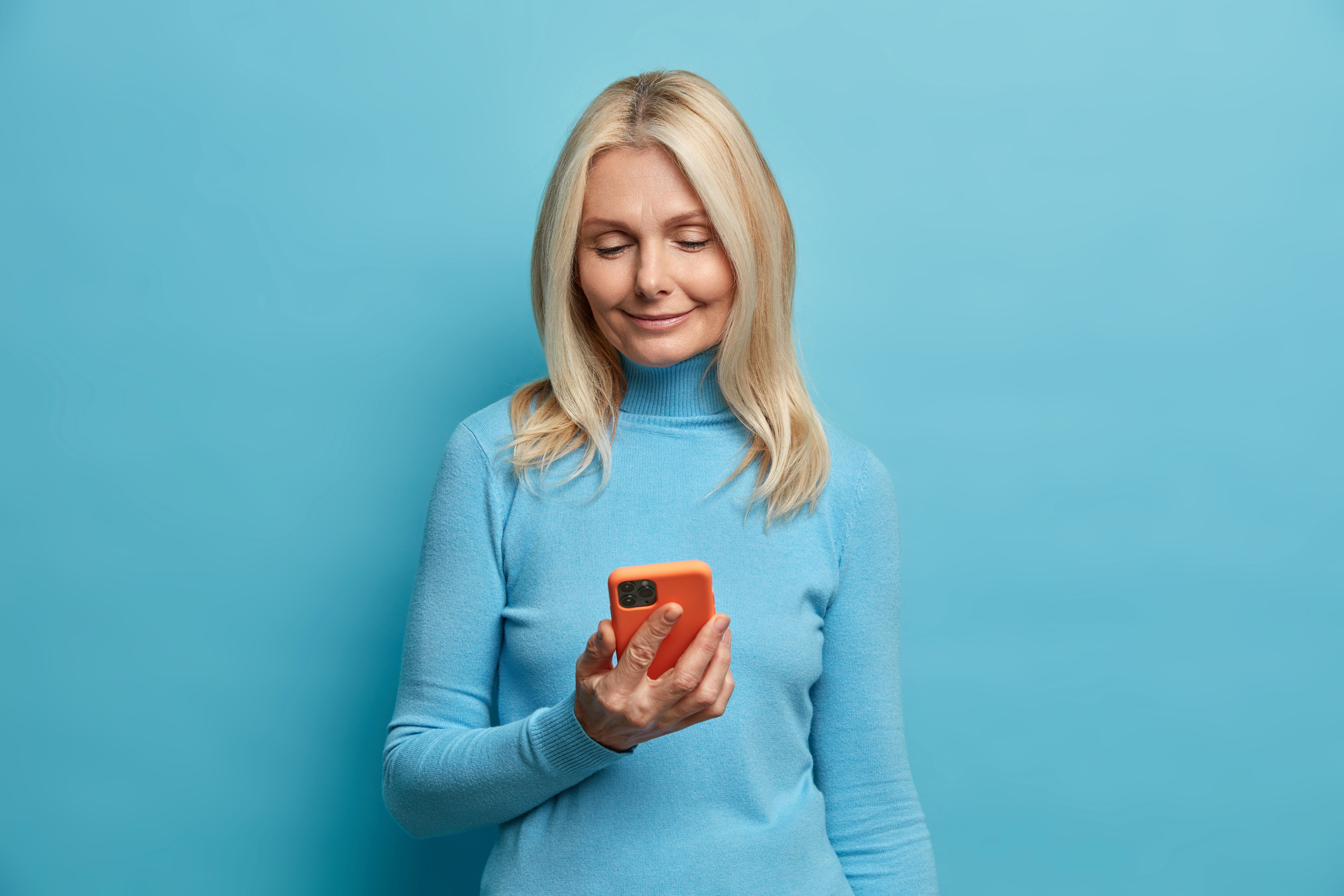 Woman with blonde hair smiles looking down at her phone