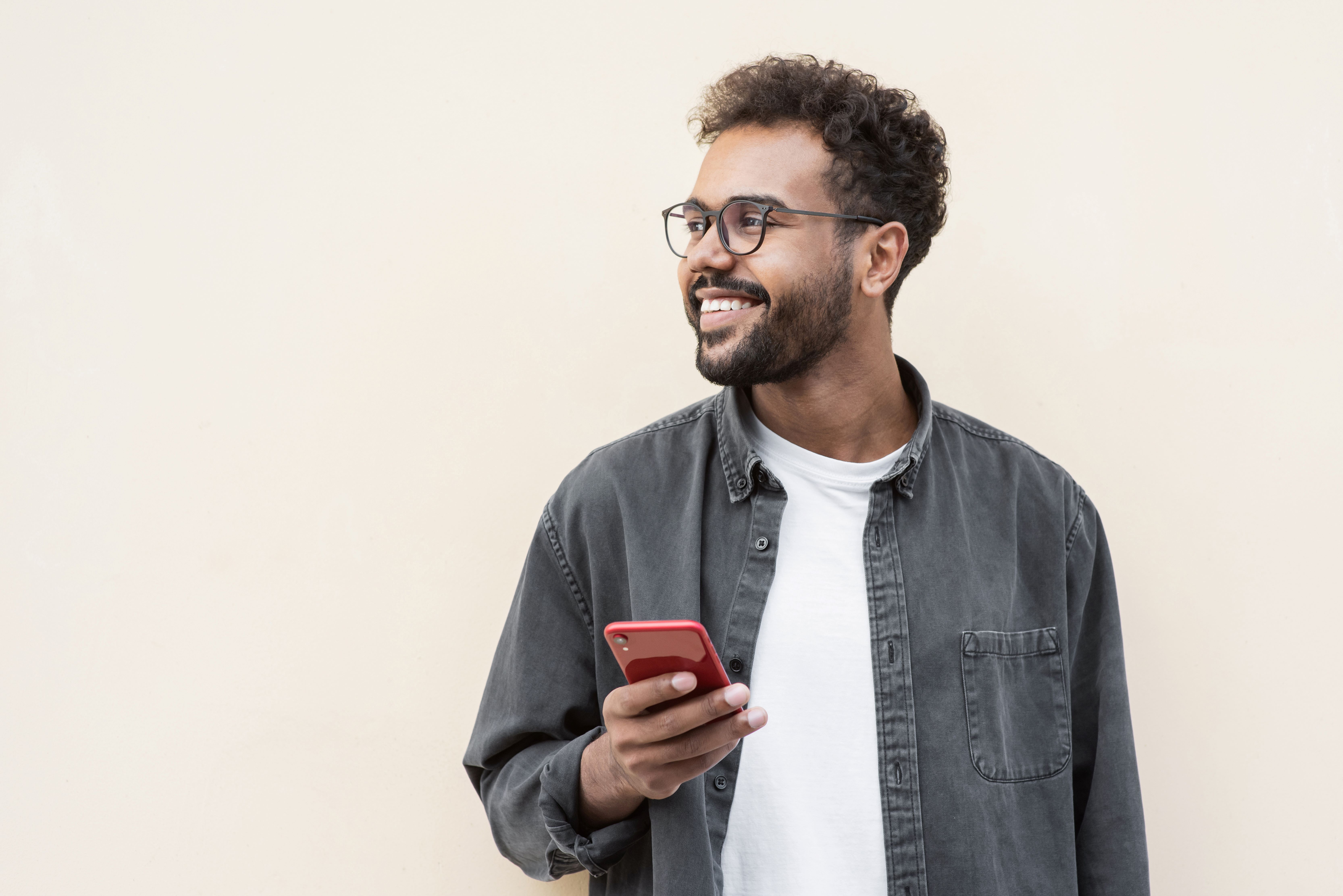 Man with brown curly hair and beard holds mobile phone and smiles looking off to his right