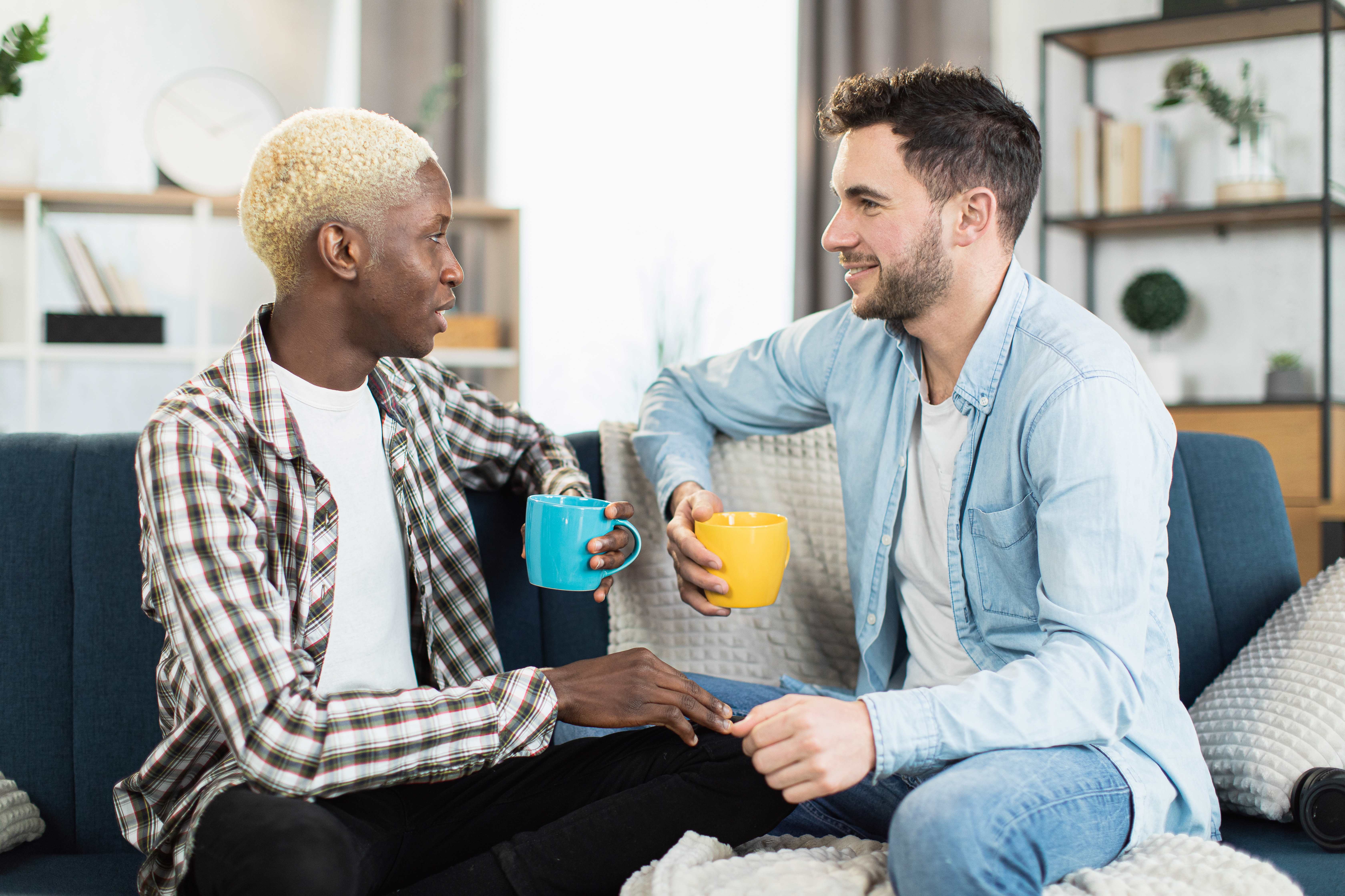 Two men holding mugs and sat chatting on a sofa