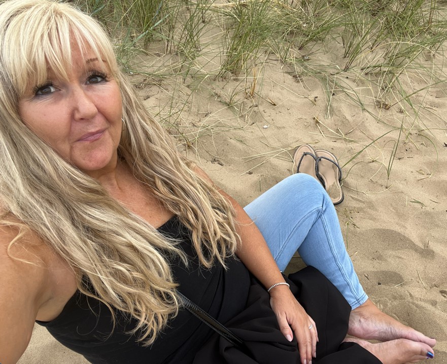 women with blond hair wearing a black top and blue jeans laying in sand dunes.