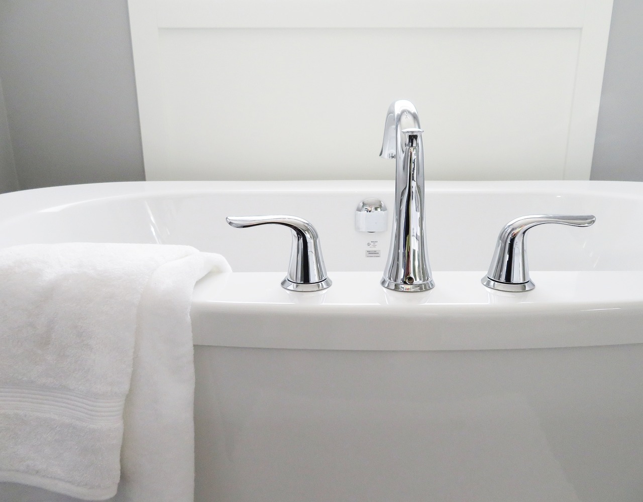 A white towel sat on the edge of a white bathtub with silver taps