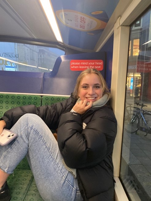 Emma sits on a bus seat with her feet up and smiles at the camera