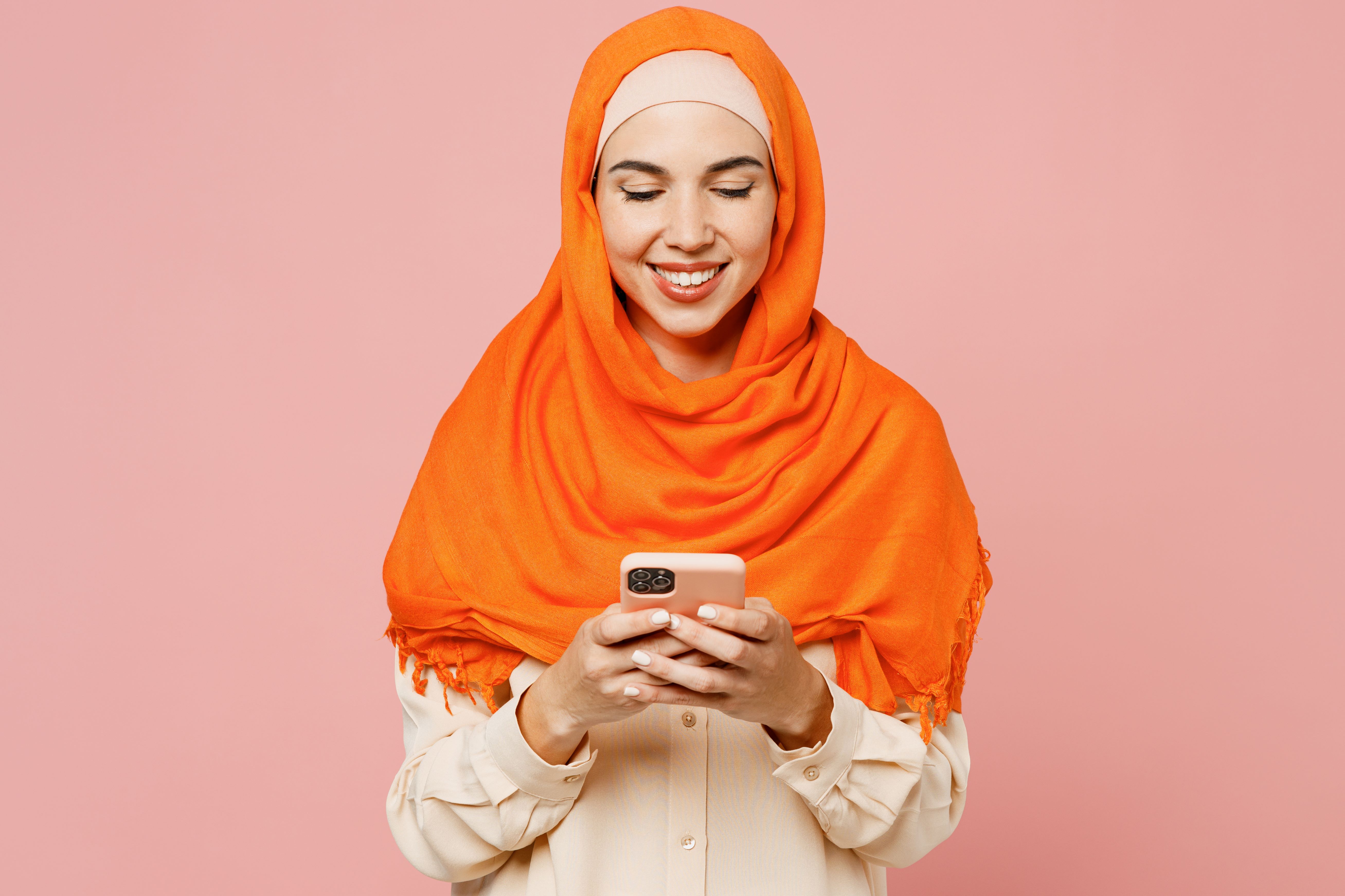 Woman in orange head scarf smiles at mobile phone