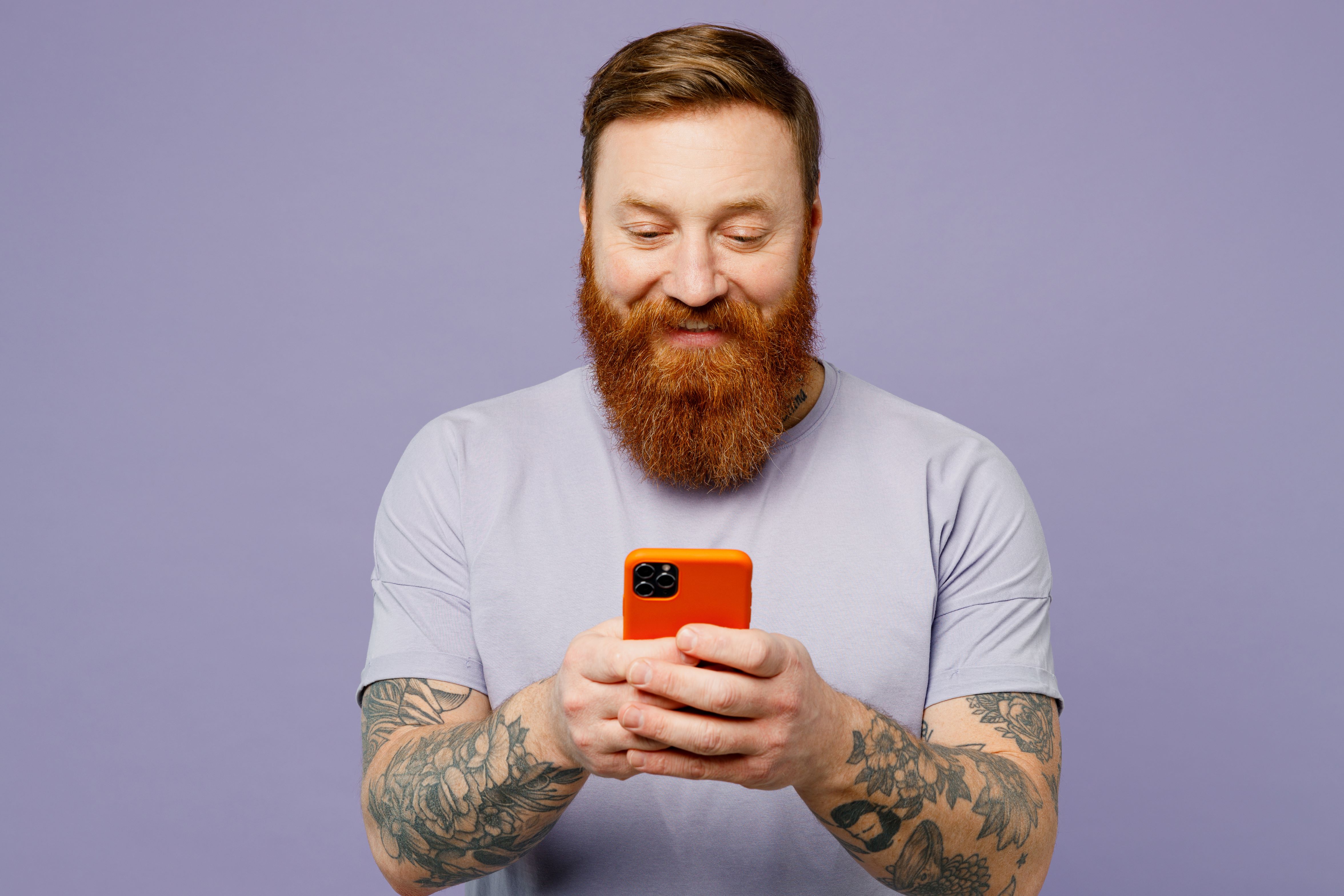 Red headed man in white t-shirt smiles at his phone