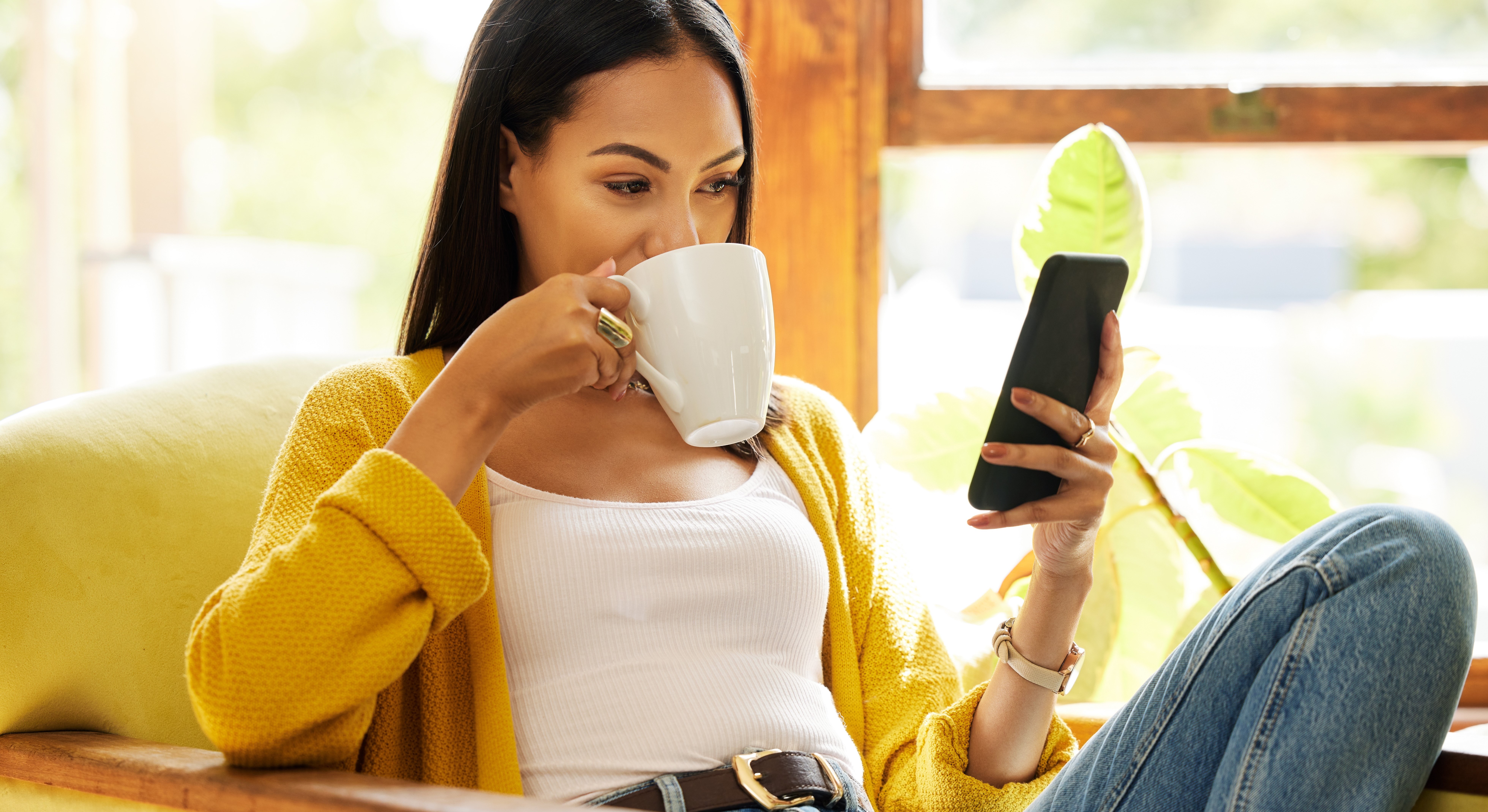 Woman drinking from a mug and looking at her mobile phone