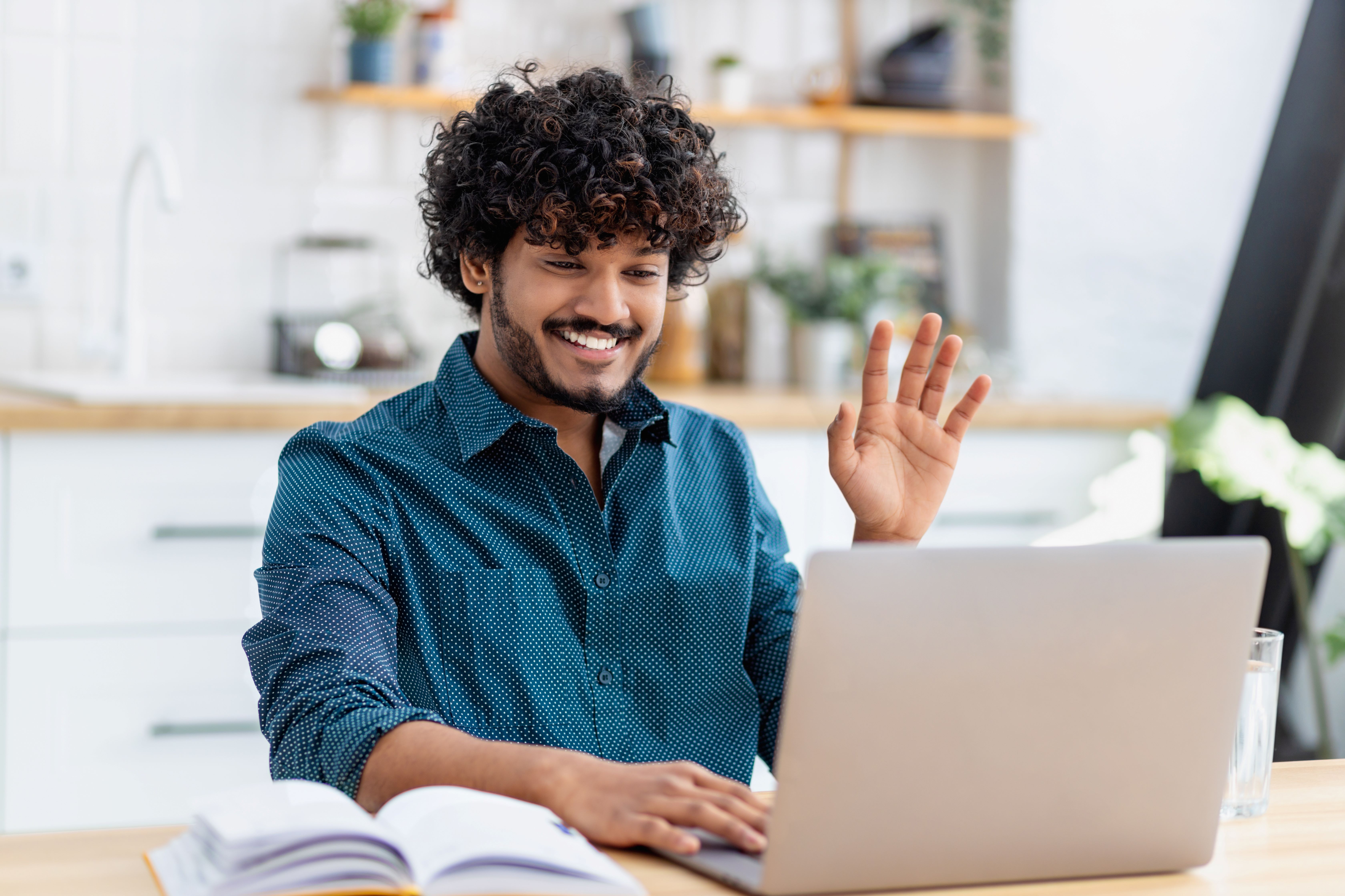 Curly haired man smiling and waving at laptop