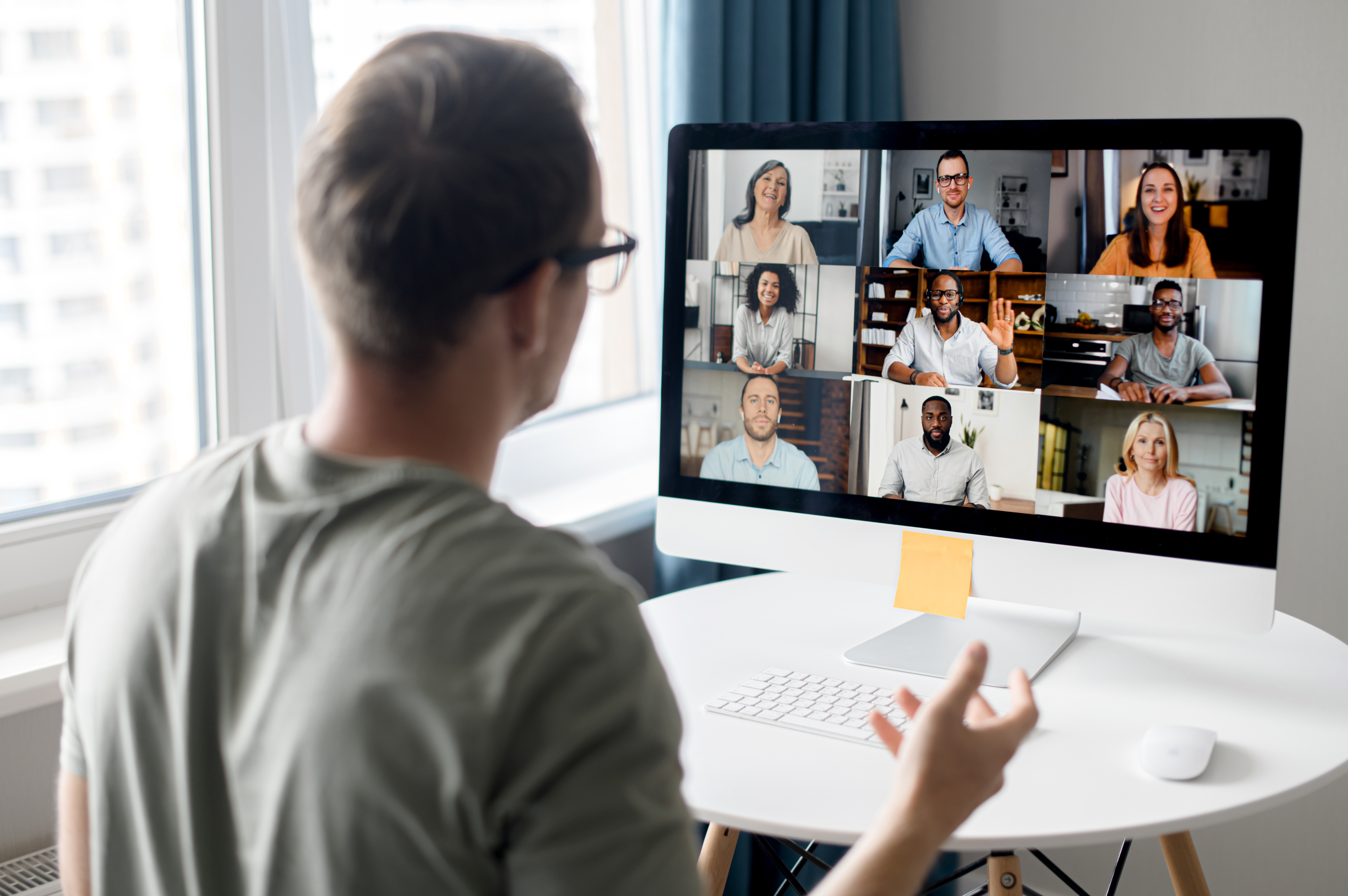 A man sitting facing his laptop in an online meeting with nine people