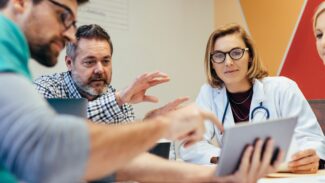 Group of health care professionals sitting around a tablet discussing something